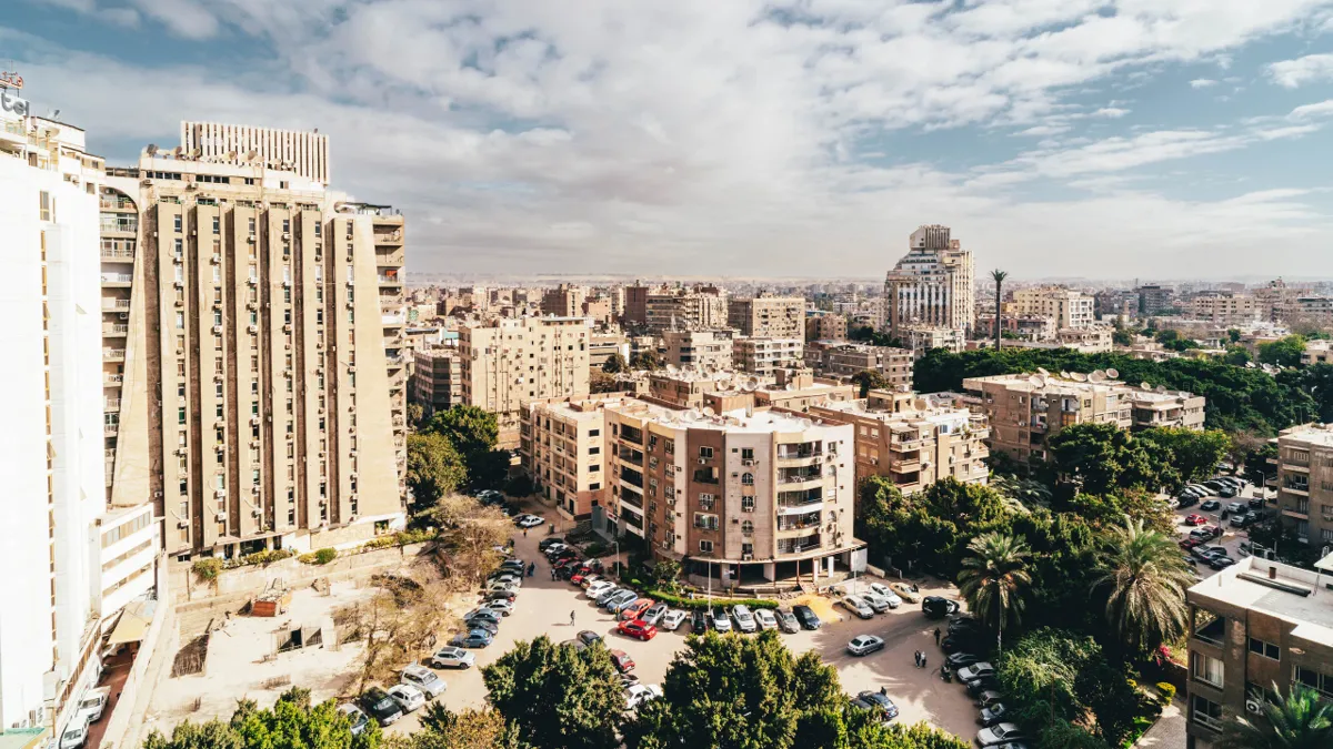 Apartment blocks and palm trees in a Cairo neighbourhood seen from above, with parked cars and scattered clouds.