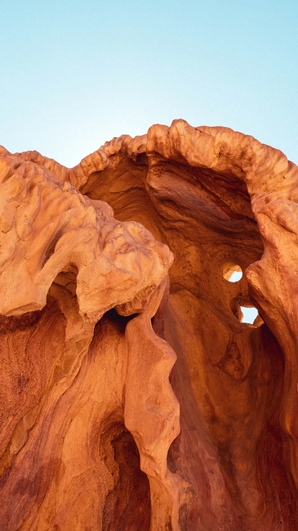 Wind-carved orange sandstone forms an arch with small openings against a clear sky in the Sinai desert.