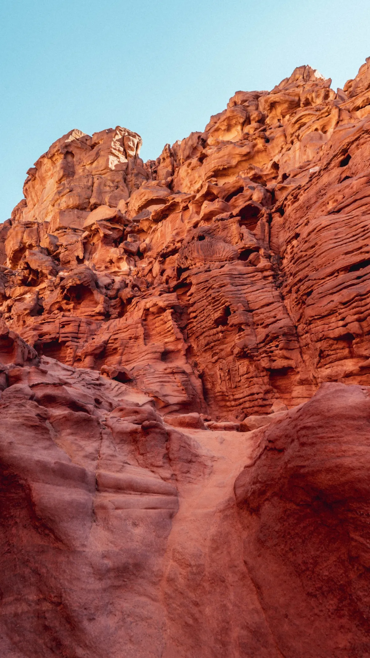 Layered, eroded red sandstone cliffs of a desert canyon rise toward a pale blue sky.
