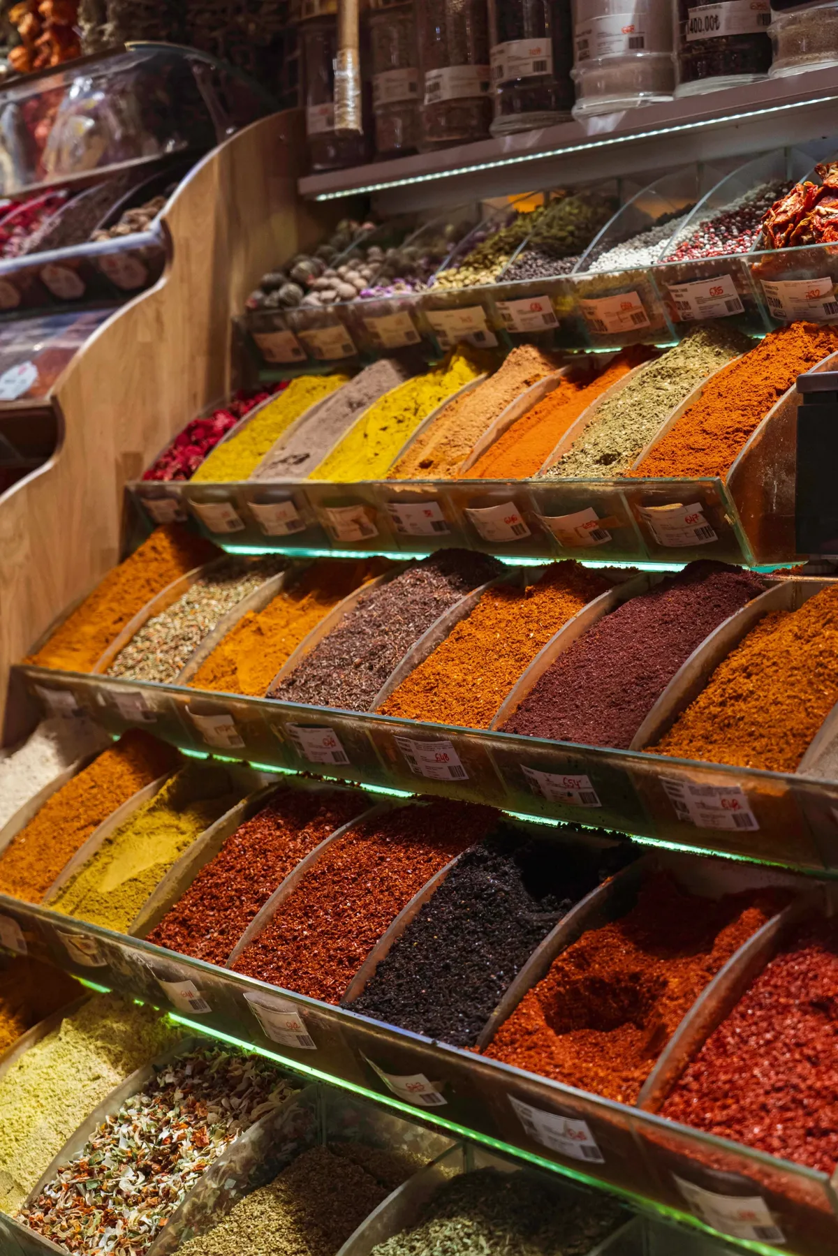Tiered bins of colourful ground spices and dried herbs with price labels at a spice stall in Istanbul.