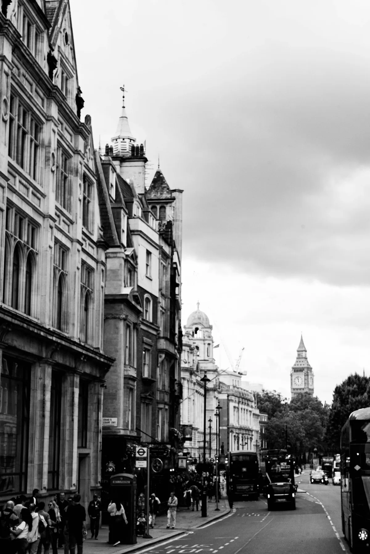 Black and white view of a London street lined with Victorian buildings, with a bus and Big Ben far ahead.
