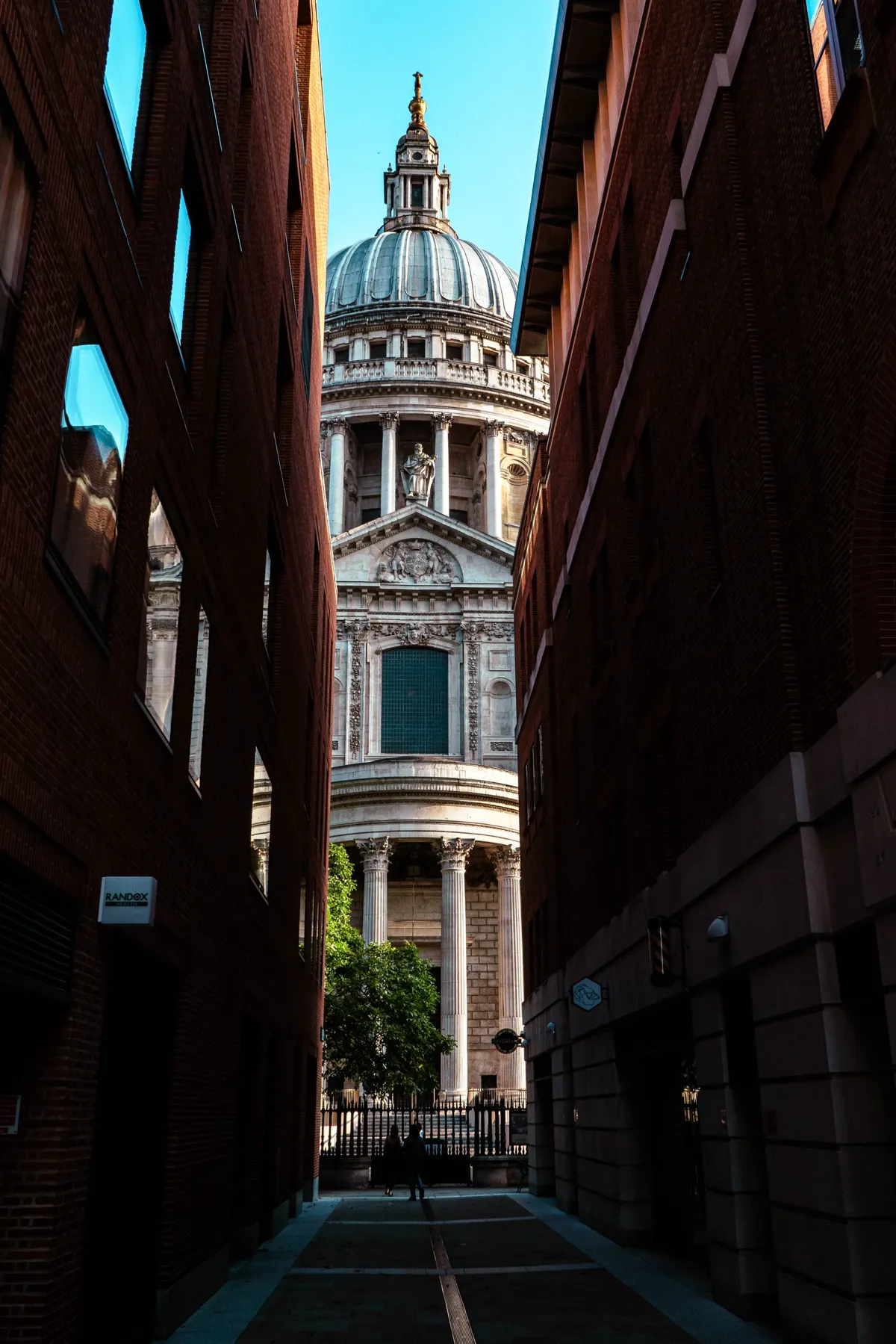 The dome and west front of St Paul's Cathedral framed by two brick buildings along a narrow London street.