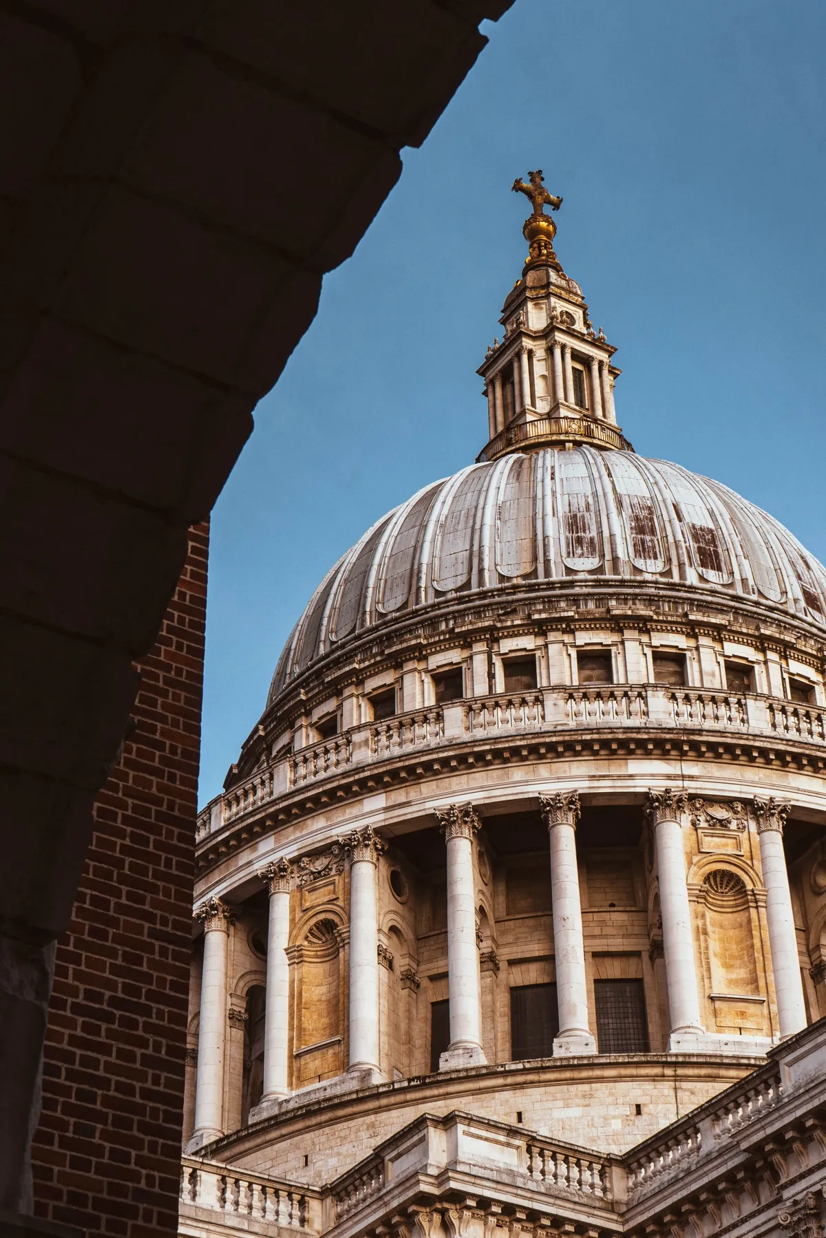 The dome and columns of St Paul's Cathedral in warm evening light, framed by a dark stone arch.