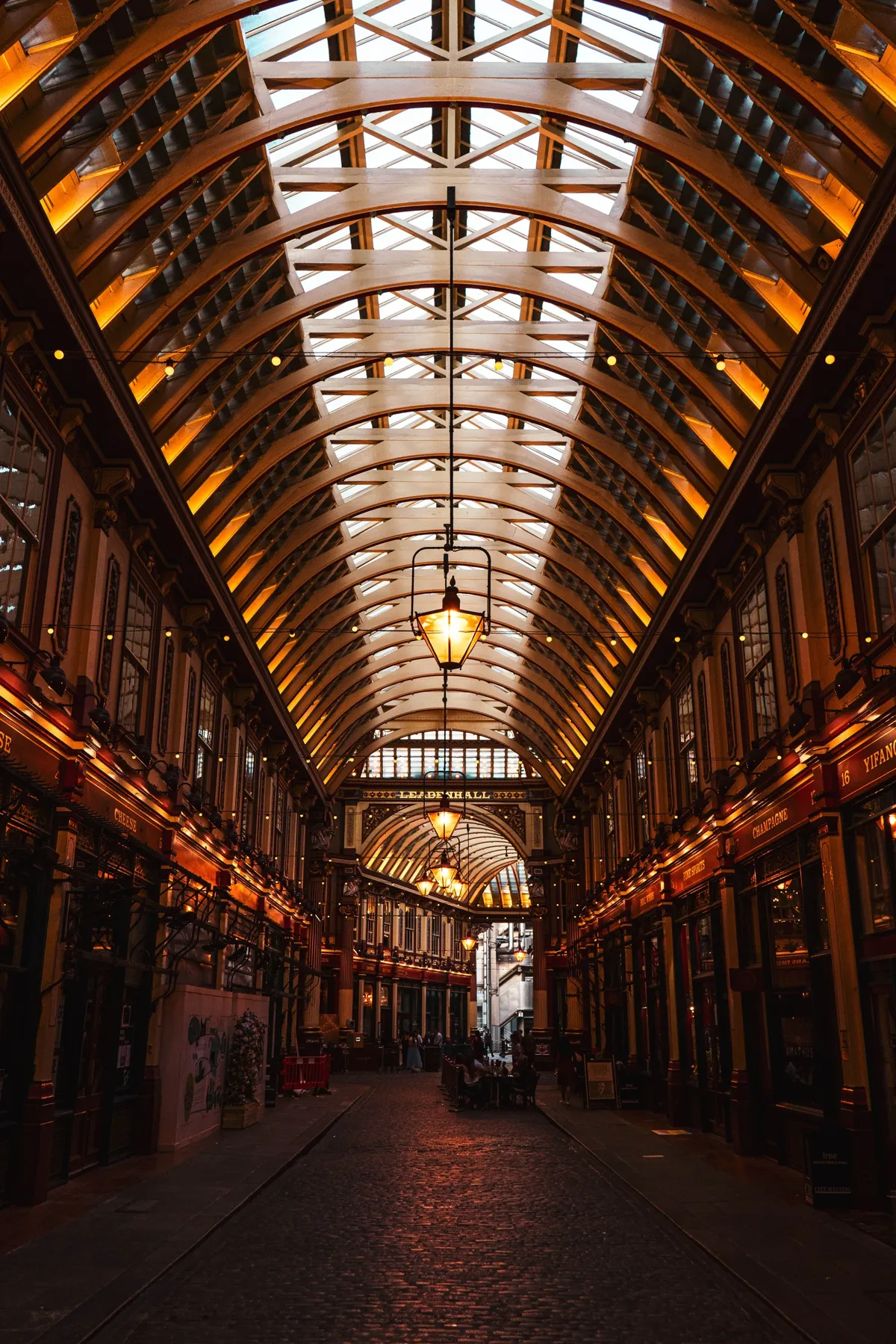 The cobbled passage of Leadenhall Market in London, with a glass and iron arched roof and hanging lanterns.