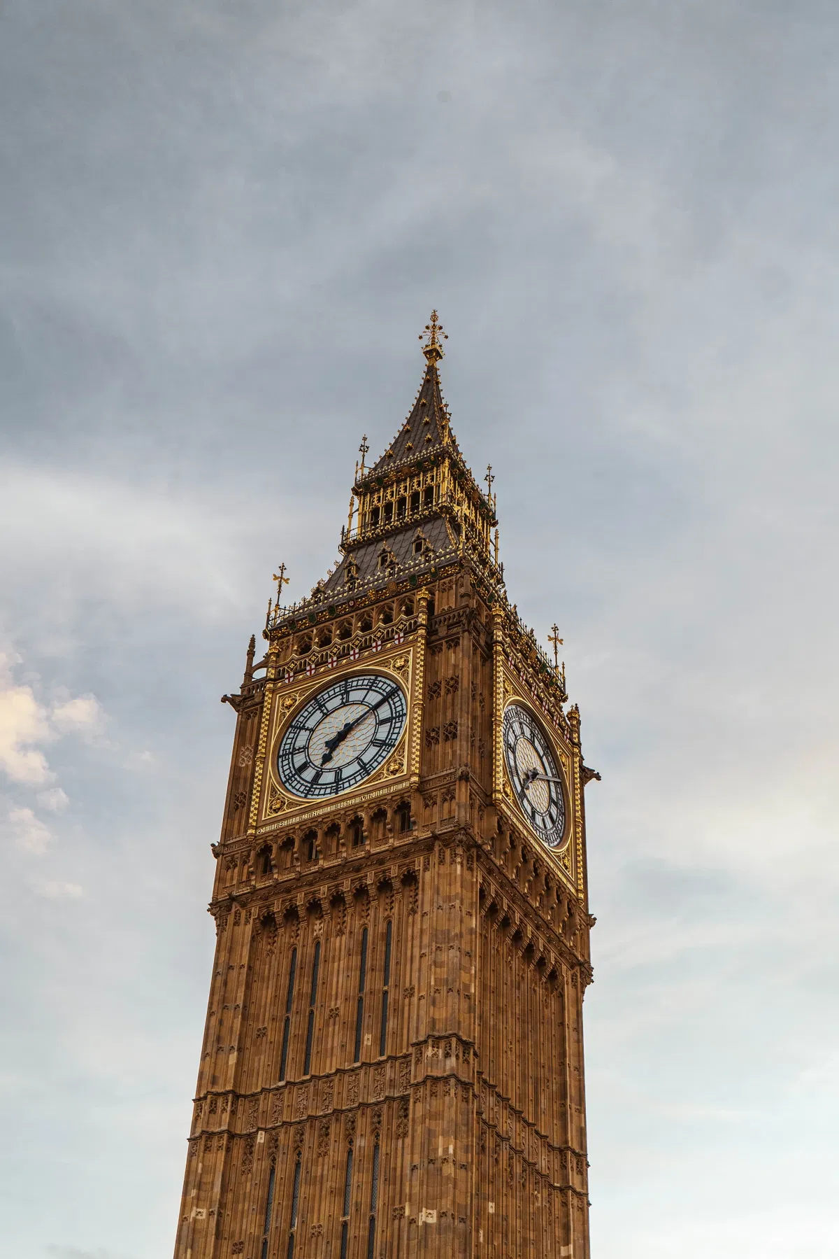 Close view of the Big Ben clock tower in London, with its golden clock faces against a cloudy sky.