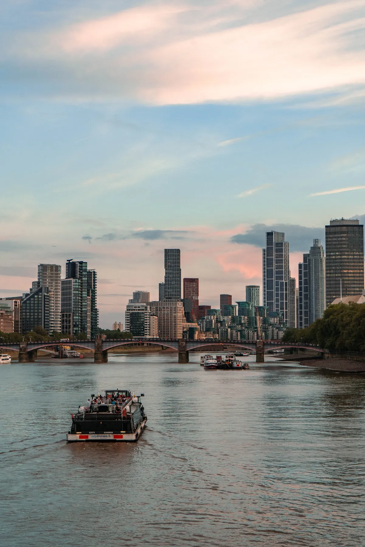 A tour boat on the Thames in London at sunset, with a bridge and modern towers on the far bank.