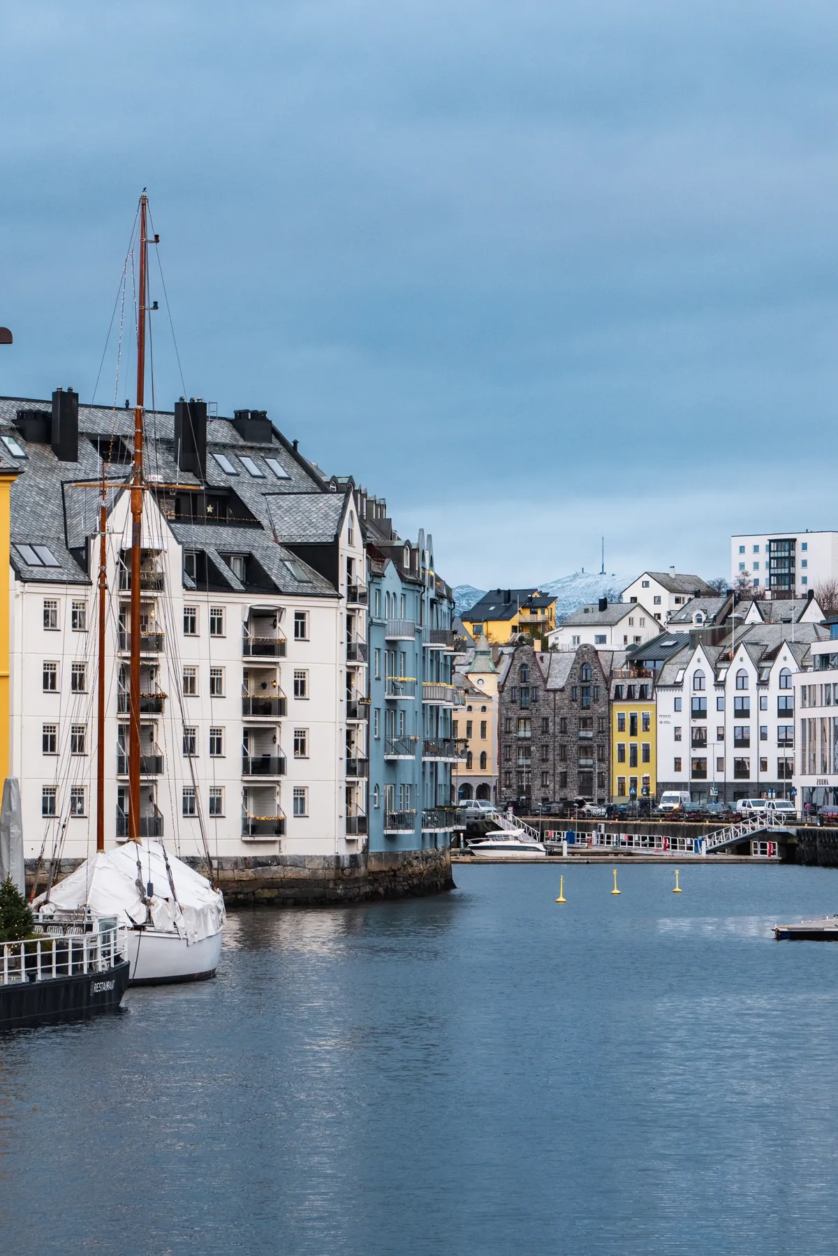 A harbour canal lined with tall Art Nouveau buildings, a sailing ship moored at left, under a cloudy evening sky.