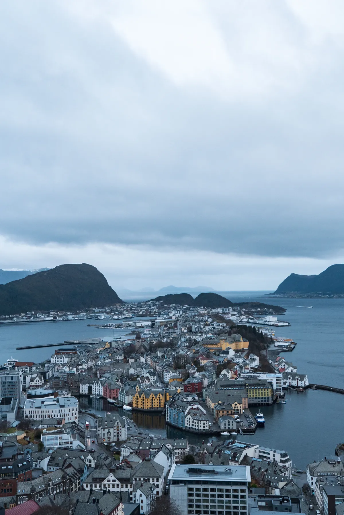 Aerial view from a hilltop over a coastal town of colourful buildings spread across islands, under overcast skies.