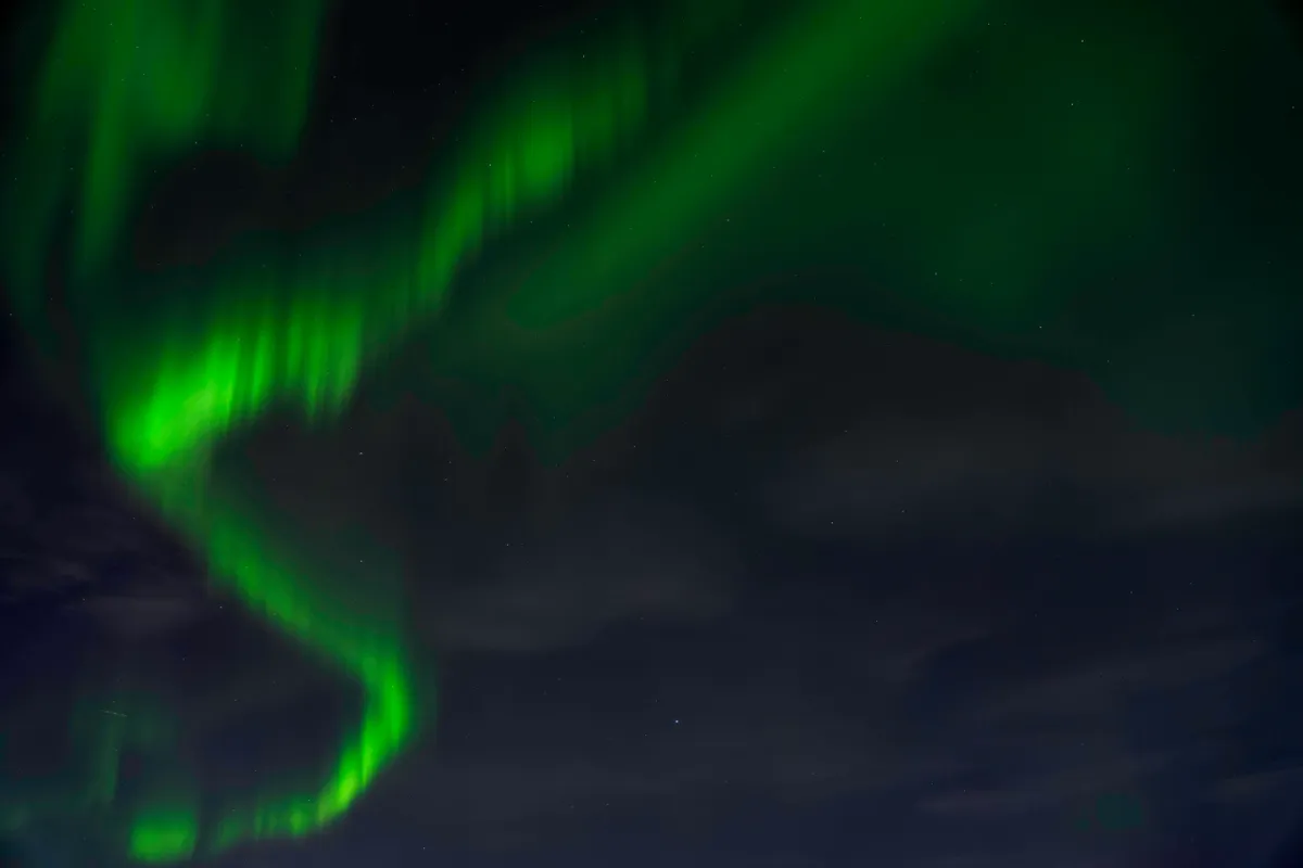 Swirling bands of green northern lights curl across a dark night sky with thin clouds.