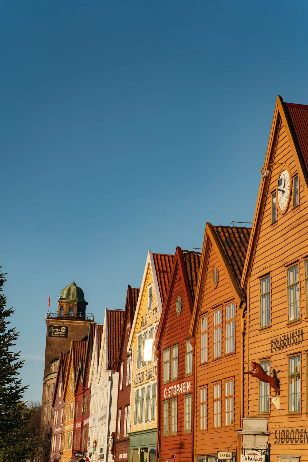 A row of orange and red wooden houses on Bryggen in Bergen, lit by low sun against a blue sky.