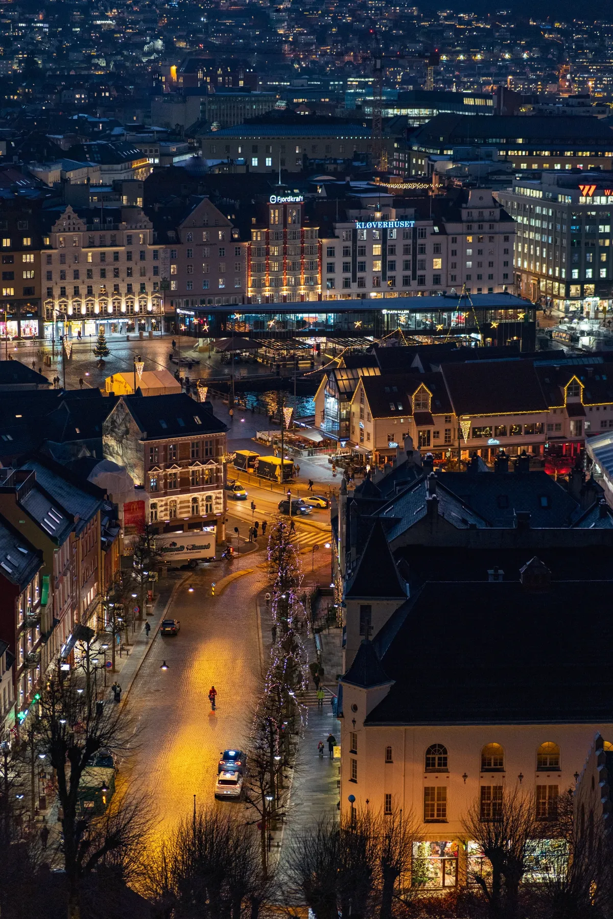 Night view from above over Bergen's old town streets, glowing with Christmas lights, with a few people walking.