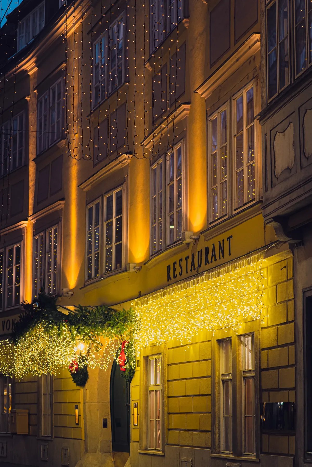 The yellow facade of a restaurant in Vienna's old town, decorated with warm Christmas lights and a garland.